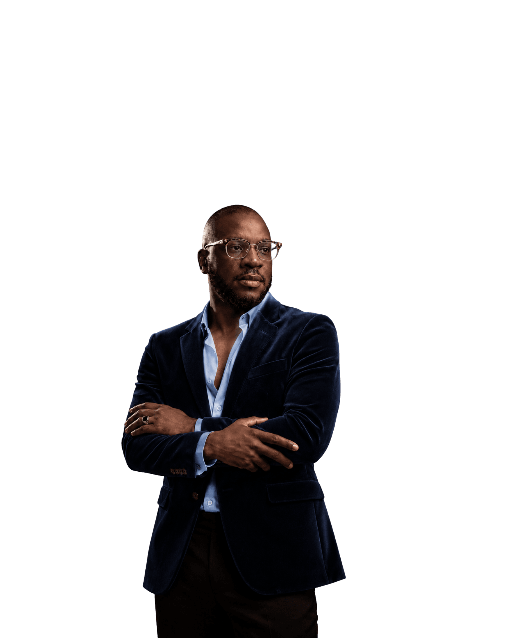 Jed Ibekwe standing with his arms crossed, in a navy velvet blazer over an open-collar shirt, a ring on his left hand